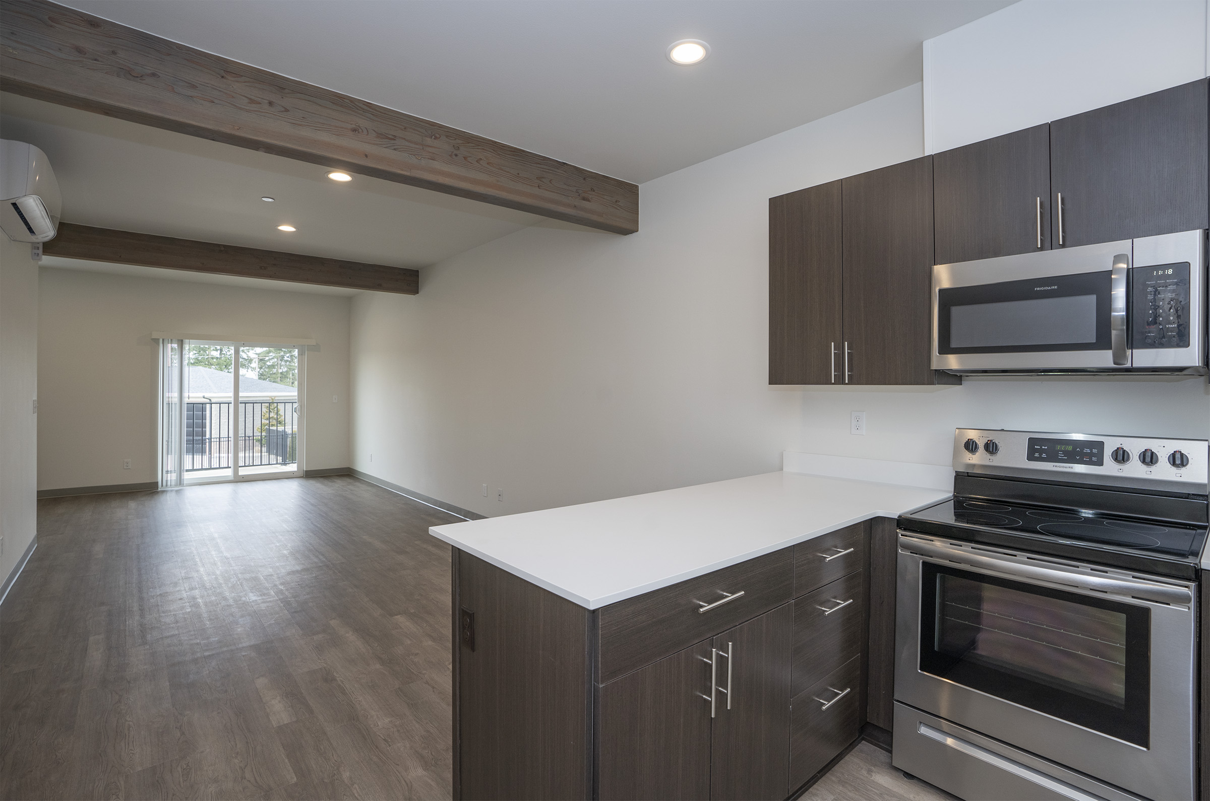 Open living area with exposed wood beams, ductless A/C, and private balcony — One-12 Townhomes